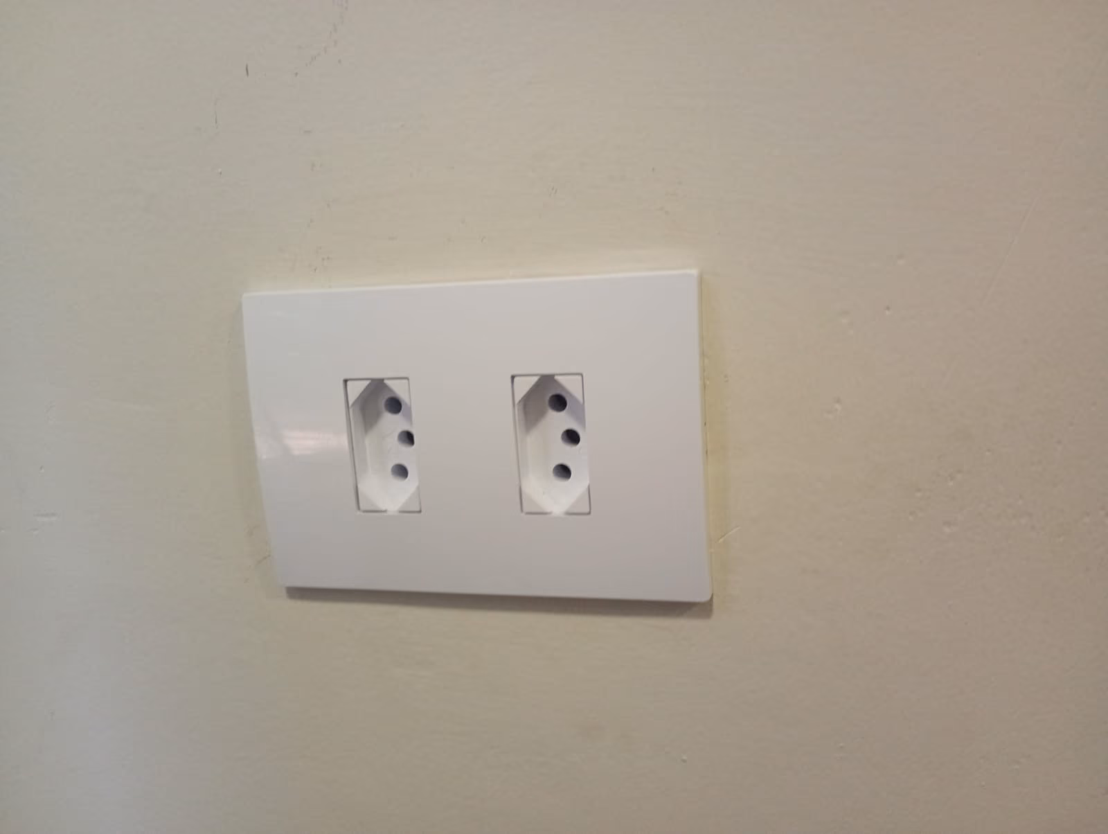 Tomada dupla instalada com espelho branco em parede de ambiente residencial