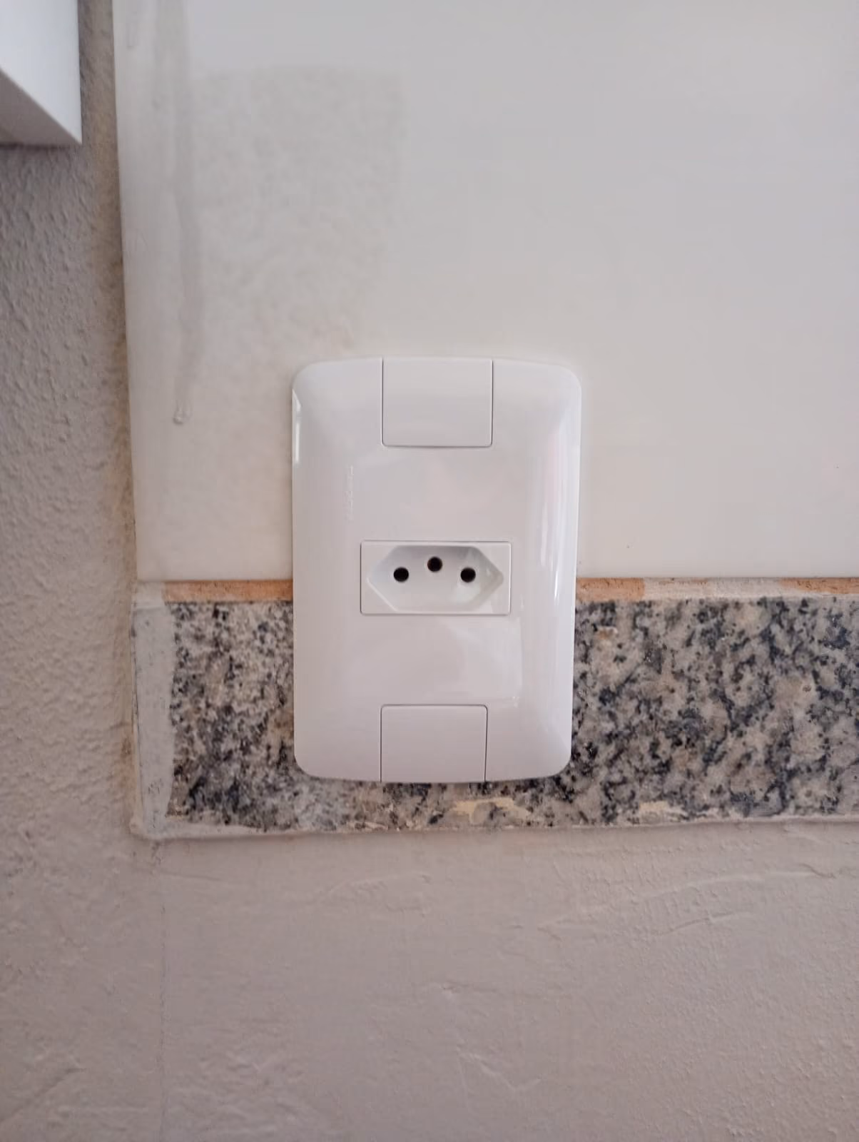 Tomada nova instalada com espelho branco em parede após a troca do ponto