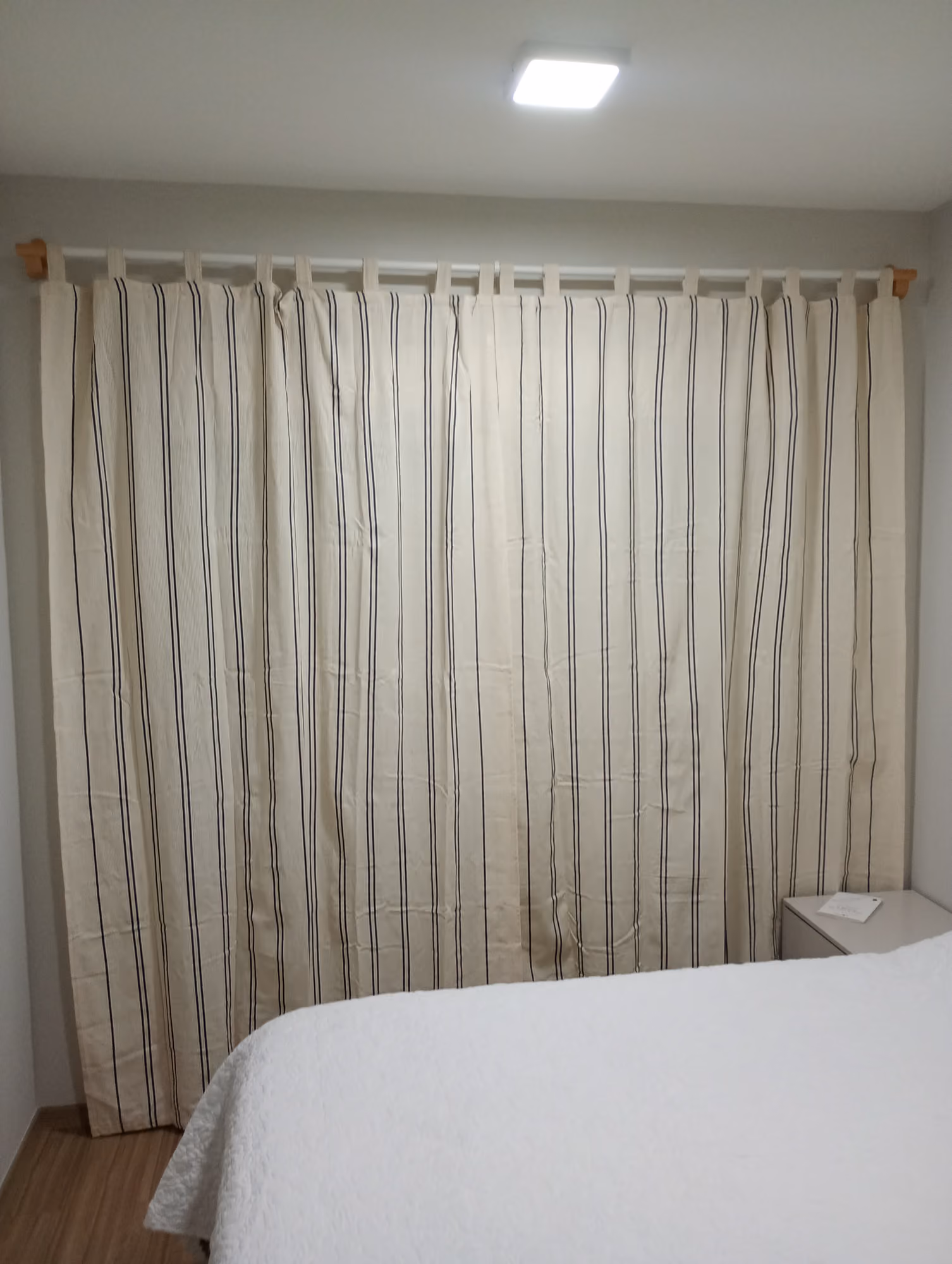 Cortina listrada instalada em varão de madeira em quarto de casal