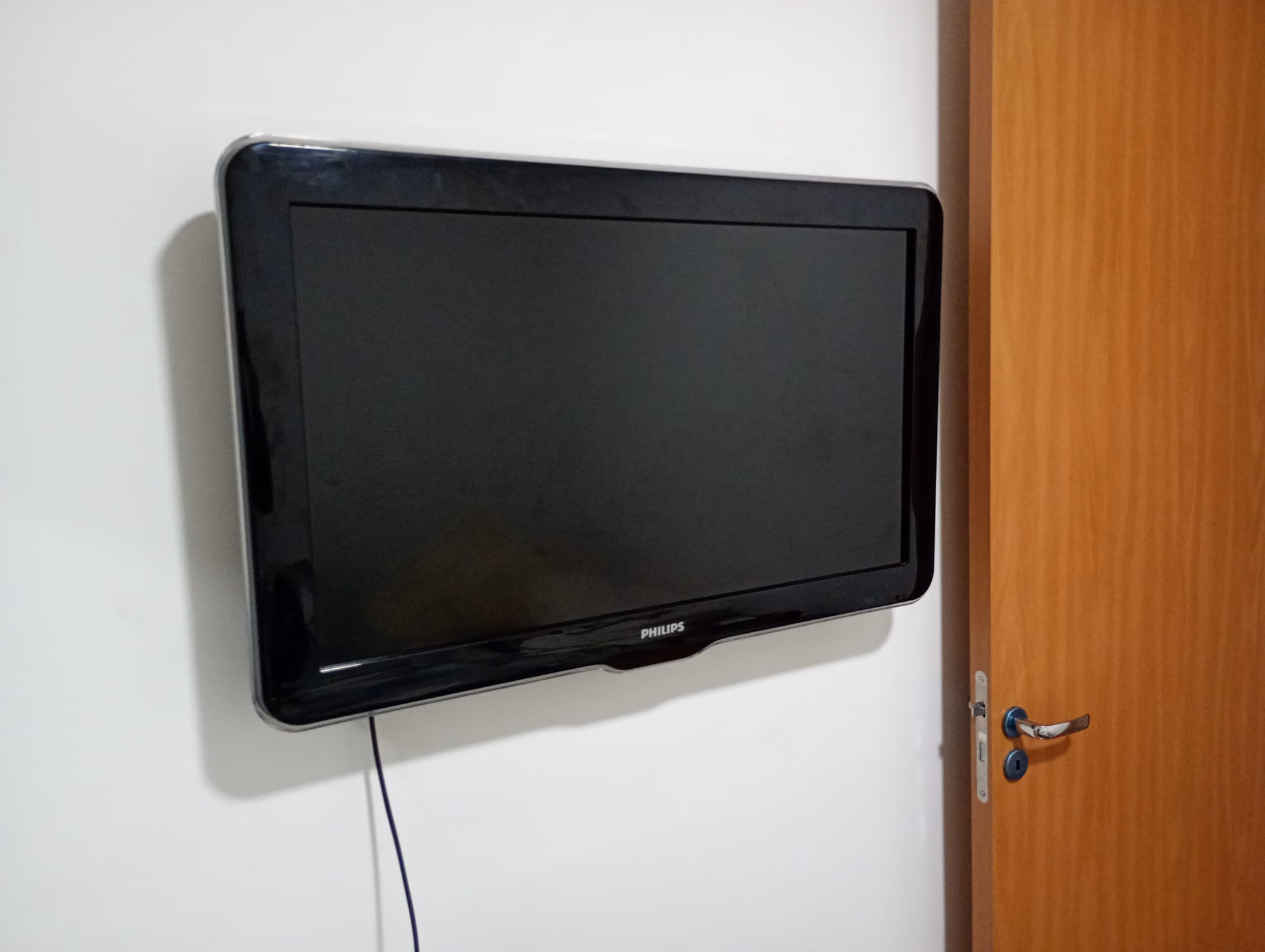 TV Philips instalada em suporte de parede ao lado da porta em quarto
